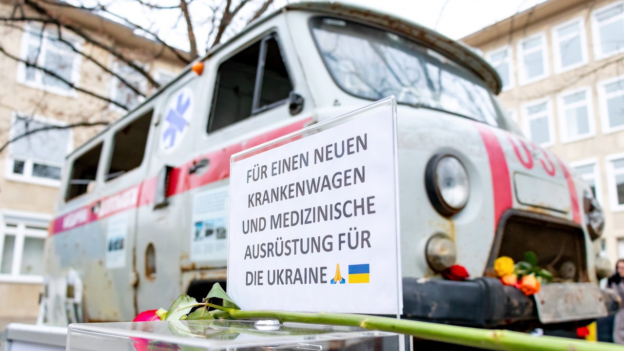 Eine durchsichtige Spendenbox mit einem Schild mit der Aufschrift:„Für einen neuen Krankenwagen und medizinische Ausrüstung für die Ukraine“. Im Hintergrund sieht man den ukrainischen Krankenwagen.
