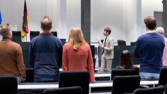 Mehrere Besucherinnen und Besucher stehen mit dem Rücken zur Kamera und sehen sich im Forum des Niedersächsischen Landtages um, während ein Landtagslotse neben dem Redepult steht und in den Raum deutet.
