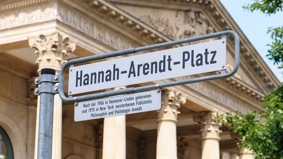 Foto eines Straßenschildes mit der Aufschrift "Hannah-Arendt-Platz" mit dem Portikus des Niedersächsischen Landtages im Hintergrund