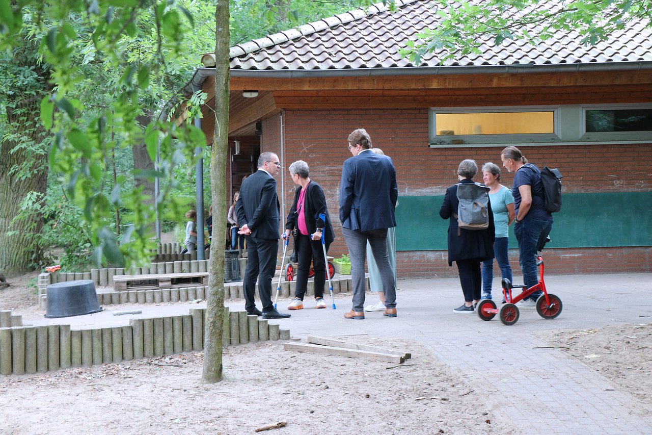 Landtagspräsidentin Naber und weitere Personen im Garten einer KiTa, rechts steht ein rotes Dreirad.