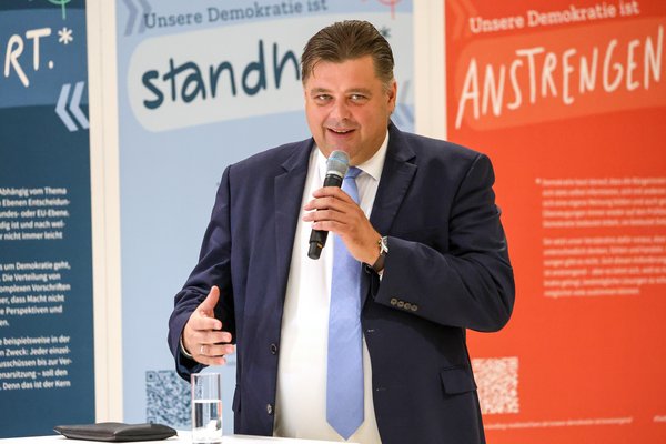 Klick auf das Bild öffnet eine vergrößerte Ansicht in einem Overlay. Zum Schließen des Overlays die ESC-Taste drücken. Landtagsvizepräsident Jens Nacke vor Aufstellern in Blau- und Orangetönen.'}