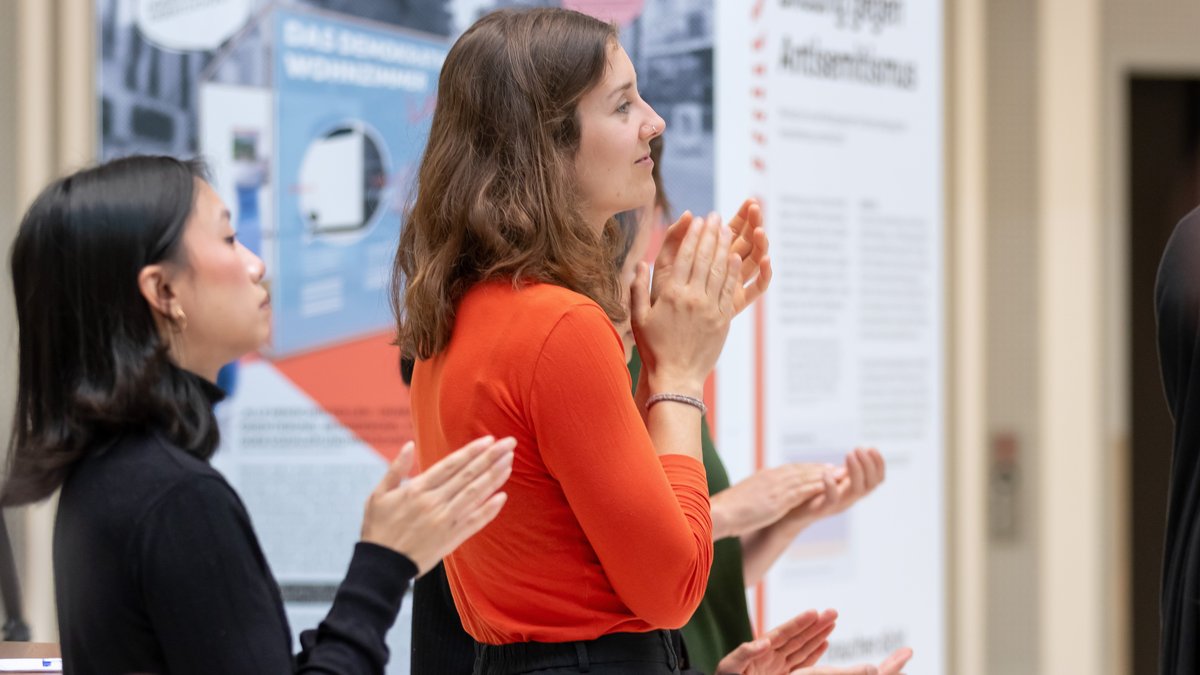 Studierende klatschen, im Hintergrund sind die Ausstellungswände zu sehen.