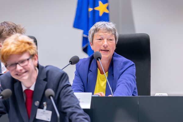 Bild: © Niedersächsischer Landtag Landtagspräsidentin Hanna Naber auf der Präsidiumsbank im Forum. Im Vordergrund ist ein grinsender Jugendlicher am Redepult zu sehen, im Hintergrund die EU-Flagge.