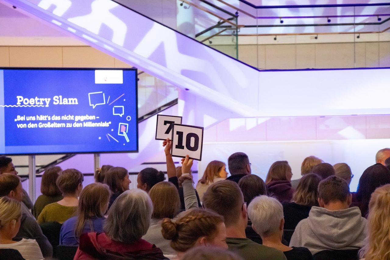 Poetry Slam 2021 im Landtag Bild: © Niedersächsischer Landtag Aus der Publikumsmenge ragt eine Hand, in der sich eine Punktekarte befindet.