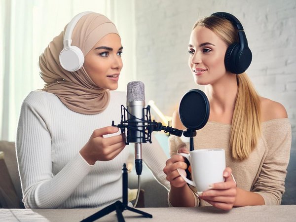 Bild: © Maryam Argat, Samar Feridhi, Sira Bohlmann (KI-generiertes Bild) KI-generiertes Bild: Zwei Frauen mit Kopfhörern an einem Mikro, eine der Frauen trägt Kopftuch.