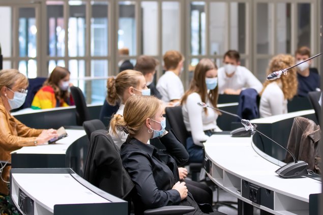 Schülerinnen und Schüler blicken sitzend auf ein Rednerpult.