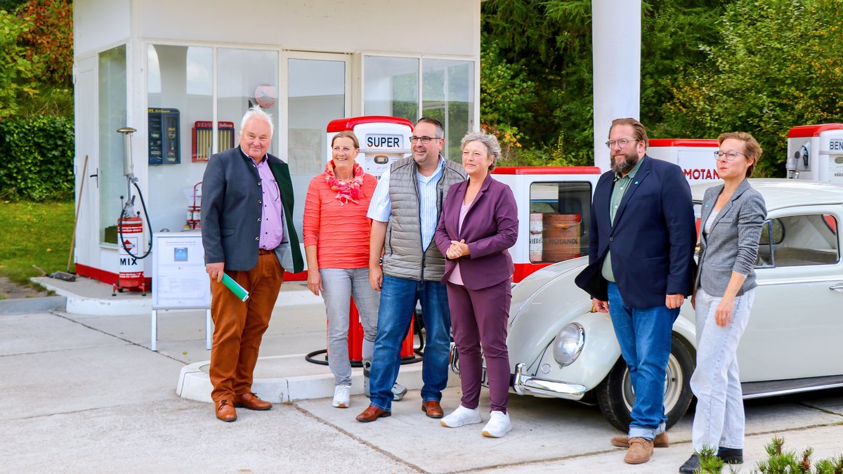 Landtagspräsidentin Hanna Naber steht mit mehreren Menschen an einer alten Tankstelle im Freilichtmuseum Kiekeberg.