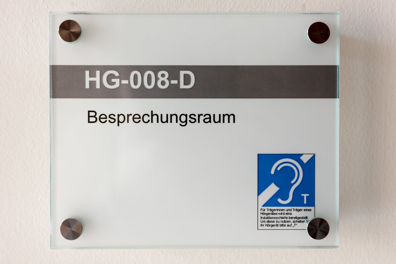 Hinweisschild auf Hörunterstützung vor einem Besprechungsraum.