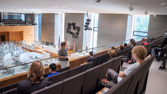 Kinder sitzen auf einer Besuchertribüne im Landtag, während eine Mitarbeiterin des Besucherdienstes erzählt.