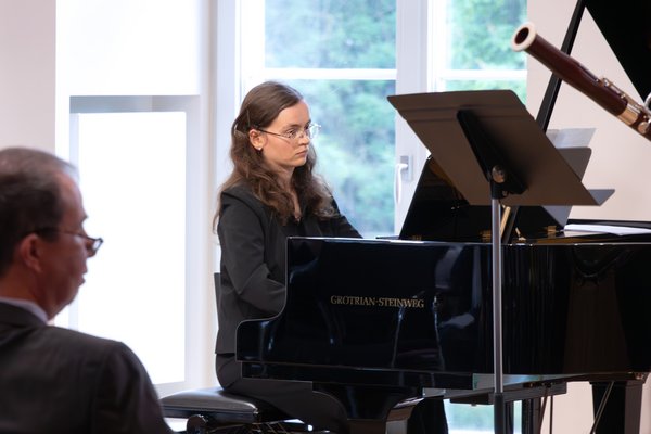 Bild: © Niedersächsischer Landtag Junge Musikerin in schwarzer Kleidung sitzt an einem Flügel und spielt Klavier, im Hintergrund ist ein Fenster zu sehen.