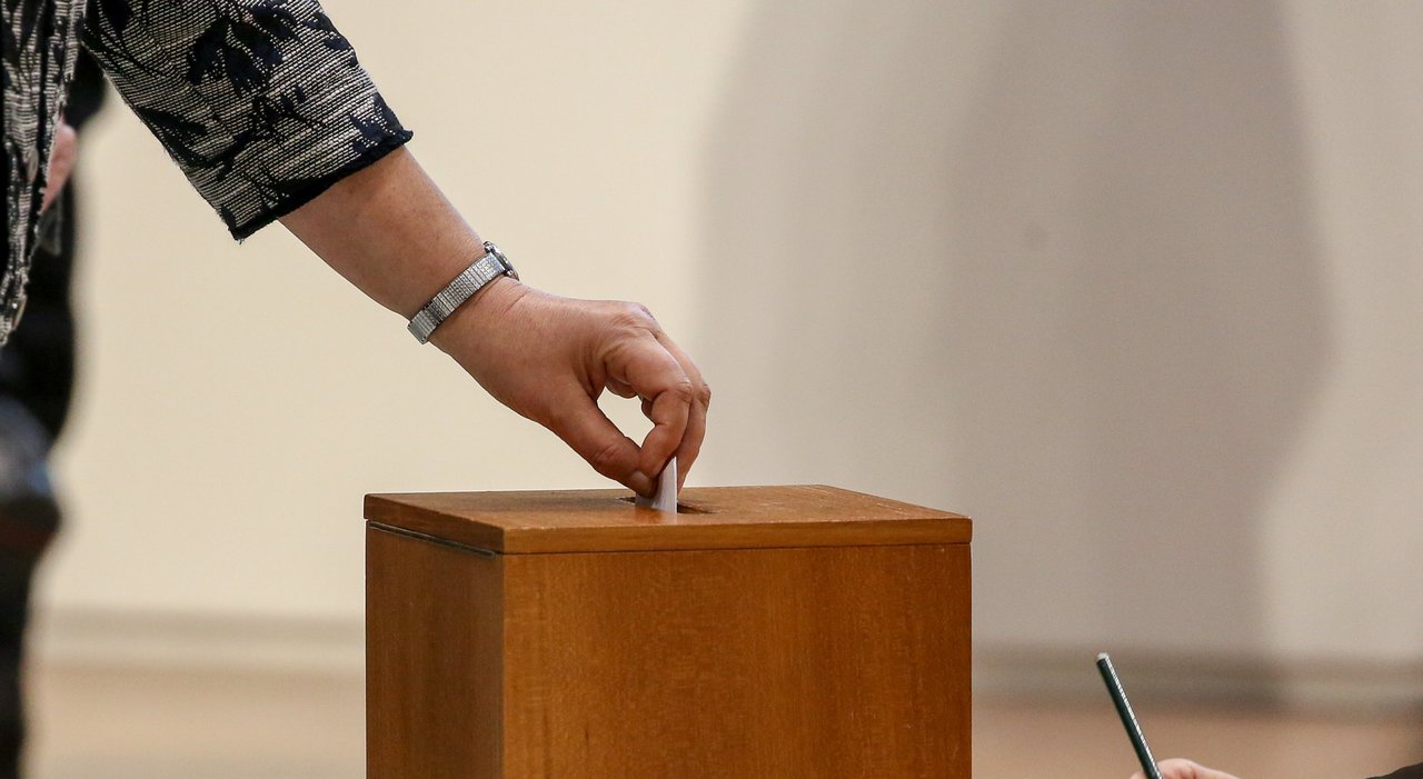 Eine Hand mit einem Stimmzettel, der in die Wahlurne gesteckt wird.