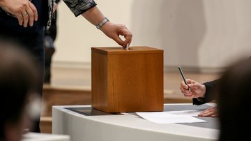 Eine Hand mit einem Stimmzettel, der in die Wahlurne gesteckt wird. Klick öffnet die Seite: Wahlprüfungsausschuss