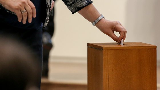 Eine Hand mit einem Stimmzettel, der in die Wahlurne gesteckt wird.
