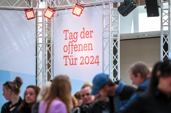 Bild: © Focke Strangmann Schriftzug "Tag der offenen Tür 2024", im Vordergrund sind unscharf einige Menschen zu sehen.