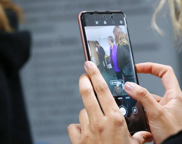 Bild: © Niedersächsischer Landtag Im Vordergrund ein Smartphone mit geöffneter Kamera-App in den Händen einer jungen Frau. Im Hintergrund die Landtagspräsidenten im Austausch mit Ehrenamtlichen.