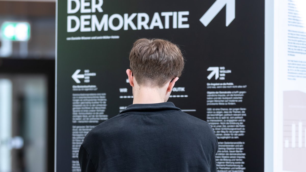Eine junge Person betrachtet das Plakat mit dem Titel „Objekte der Demokratie“