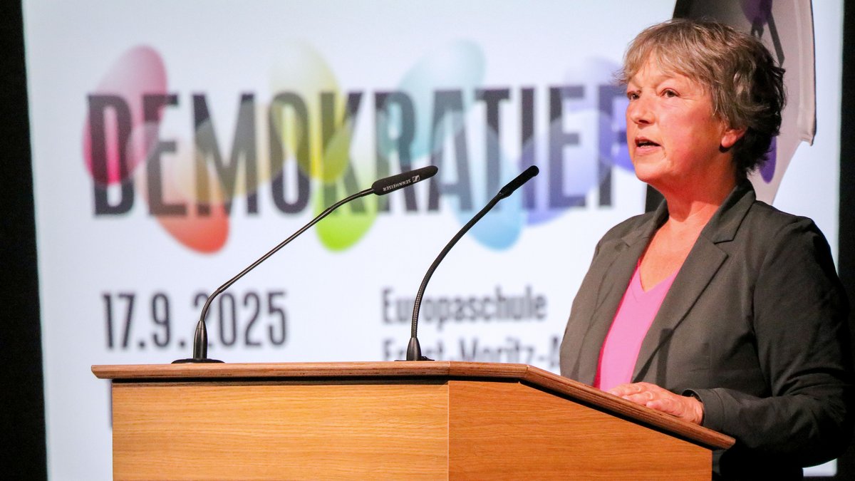 Landtagspräsidentin Hanna Naber steht an einem Redepult und spricht in zwei Mikrofone. Im Hintergrund ist eine Leinwand zu sehen, auf der zu lesen ist: "Demokratiefest 17.9.2025"