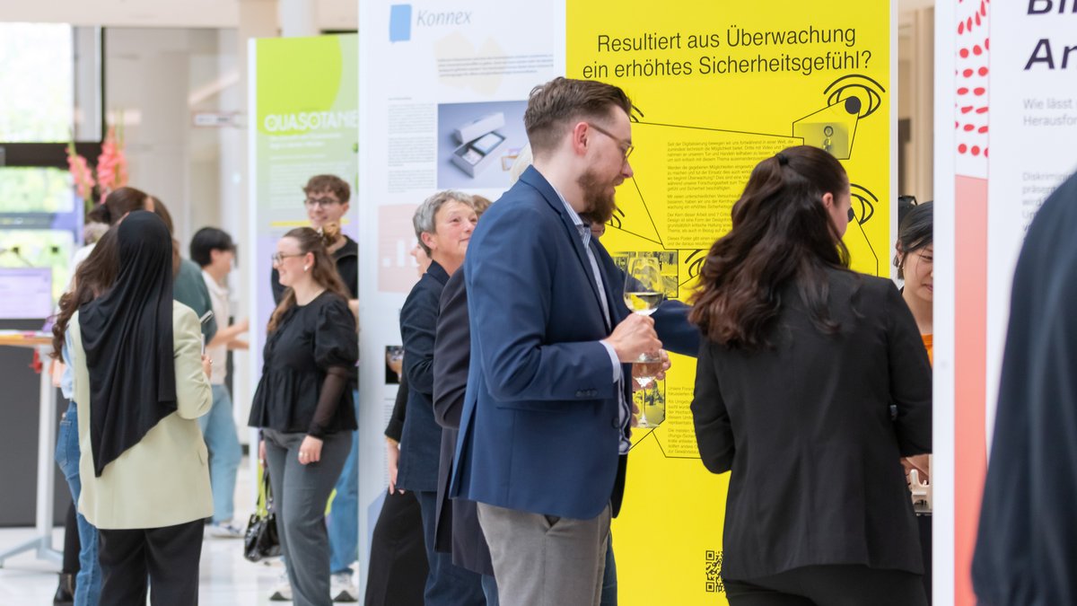 Das Publikum im Austausch mit Studierenden vor den Ausstellungswänden.