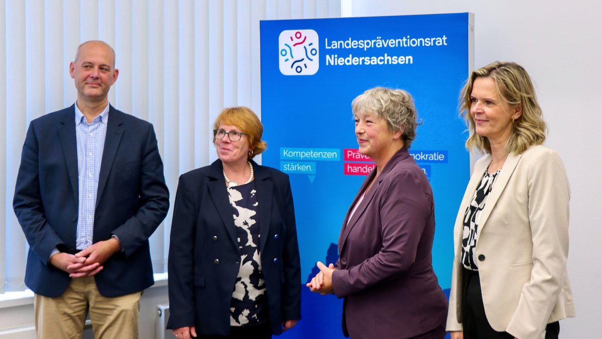 Landtagspräsidentin Hanna Naber steht mit drei Personen des Landespräventionsrates Niedersachsen zusammen. Im Hintergrund sieht man ein blaues Roll-Up mit dem Logo.