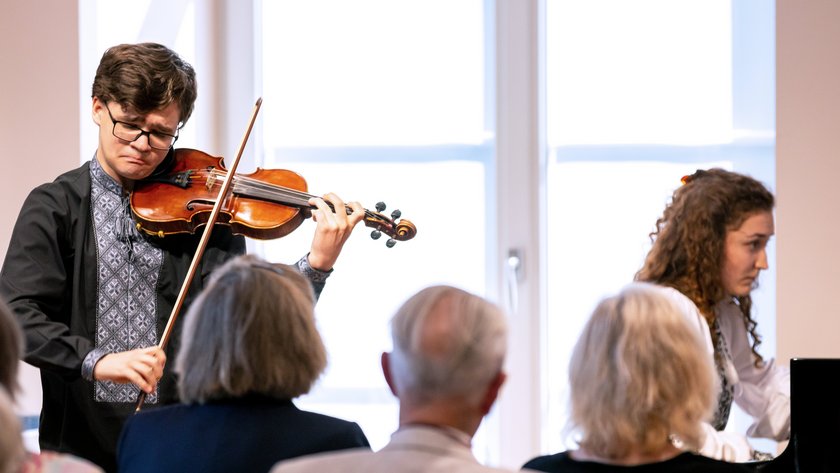 Ein Violinist und eine Pianistin spielen vor Publikum.