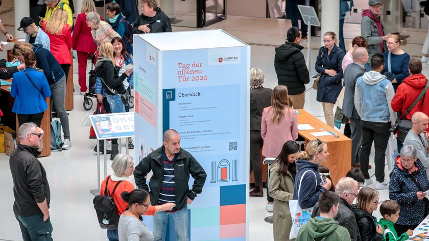 Ansicht der gut besuchten Portikushalle beim Tag der offenen Tür. In der Mitte steht eine Säule mit dem Text "Tag der offenen Tür 2024" sowie Informationen zum Programm.