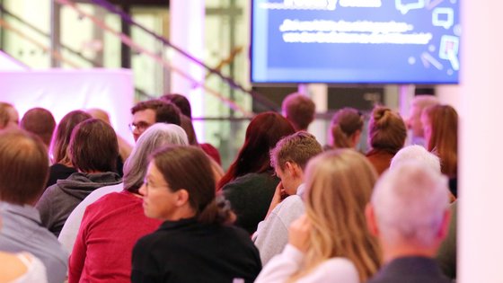 Publikum von hinten in der leicht rosa beleuchteten Portikushalle.
