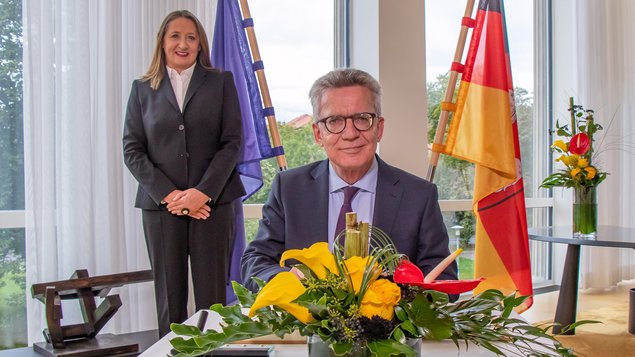 Prof. Dr. Thomas de Maizière sitzt vor dem Gästebuch, Landtagspräsidentin Andretta im Hintergrund