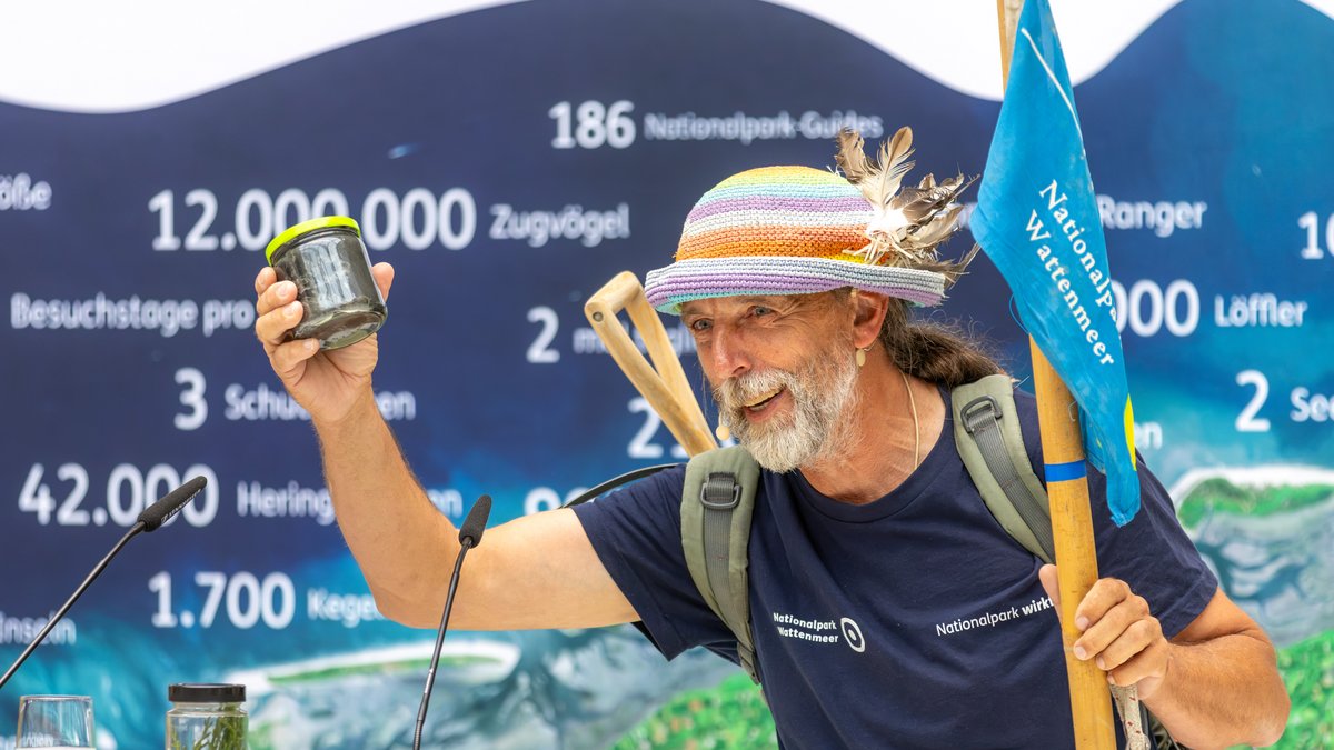 Nationalpark-Führer Joke Pouliart steht vor dem Publikum, um es durch eine etwas andere Wattwanderung zu führen und hält ein "Glas Watt" in der Hand.