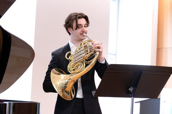 Bild: © Niedersächsischer Landtag Junger Mann in elegantem schwarzen Anzug spielt ein goldenes Horn, vor ihm steht ein Notenständer.