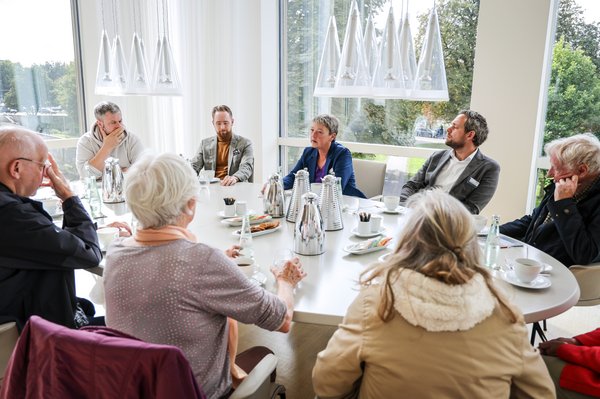 Bild: © Focke Strangmann Landtagspräsidentin Hanna Naber sitzt inmitten einer kleinen Gruppe von Besucherinnen und Besuchern am Konferenztisch in ihrem Arbeitszimmer. Auf dem Tisch stehen Kannen, Tassen und Teller mit Keksen.