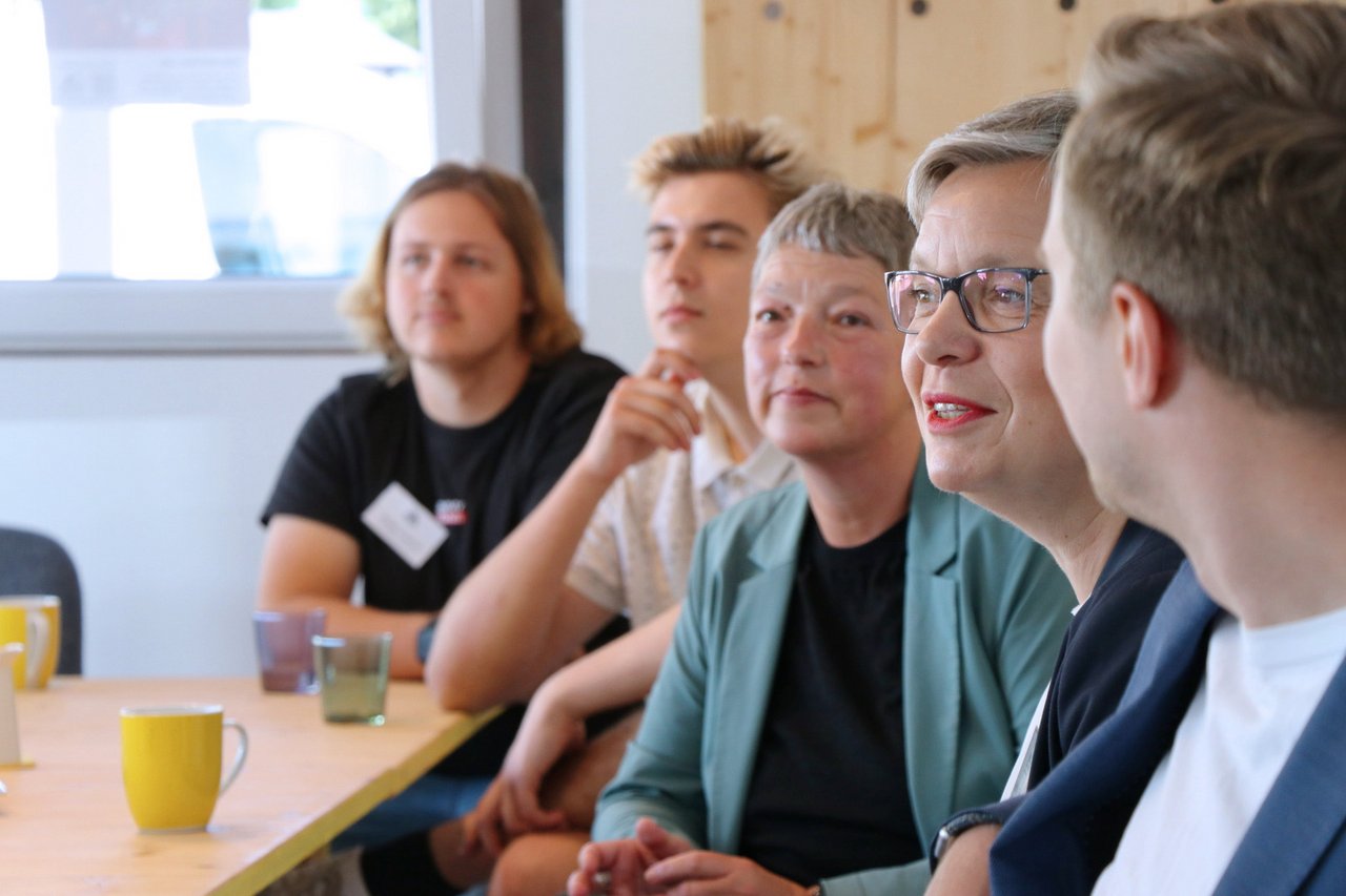 Bild: © Niedersächsischer Landtag Landtagspräsidentin Naber sitzt am Tisch zwischen anderen Menschen, im Fokus steht neben ihr Monika Dehmel von Politik zum Anfassen e.V.