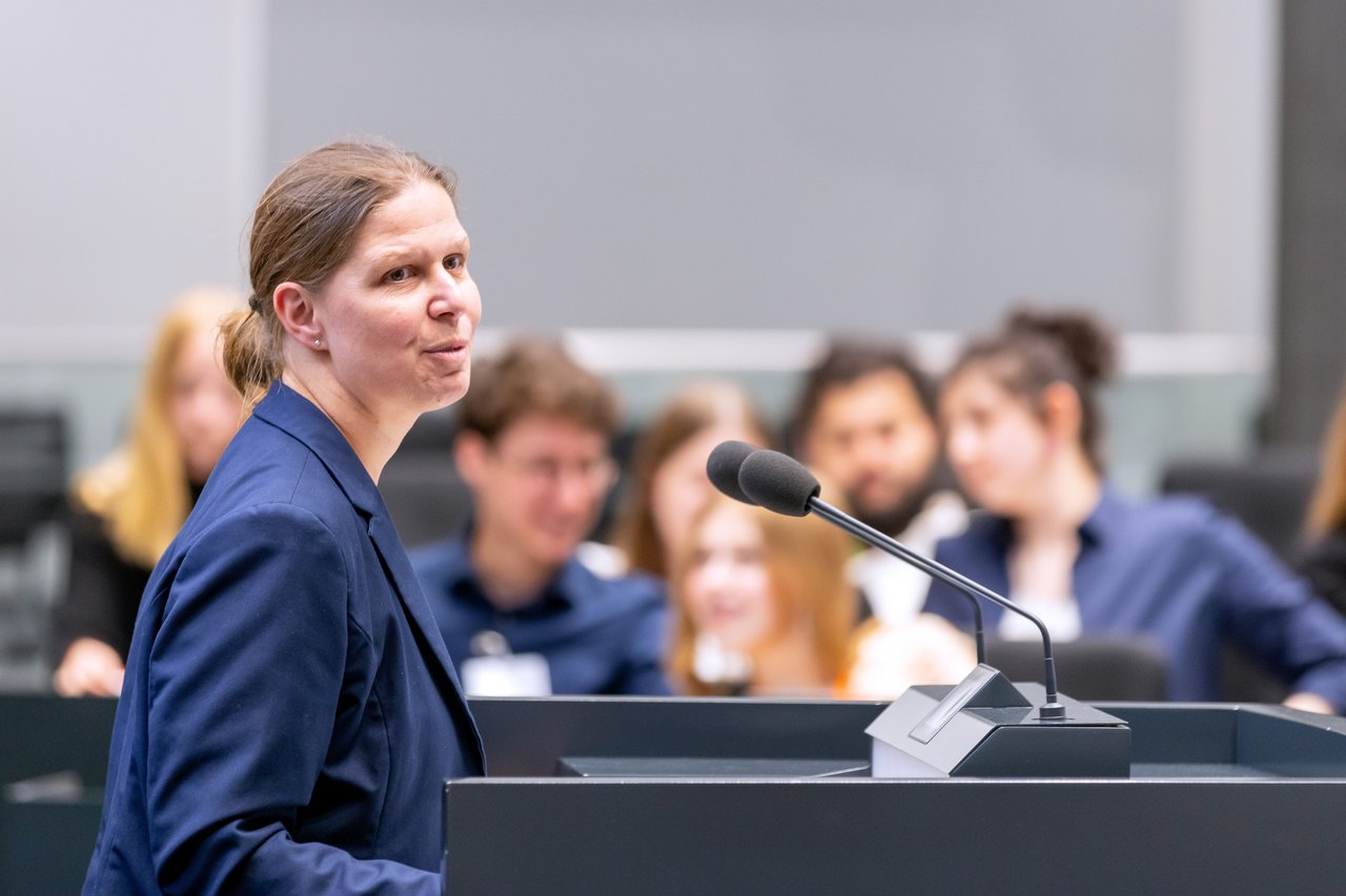 Ministerin Wiebke Osigus steht am Redepult im Forum und spricht in die Mikrofone. Im Hintergrund sind mehrere Schülerinnen und Schüler zu sehen.