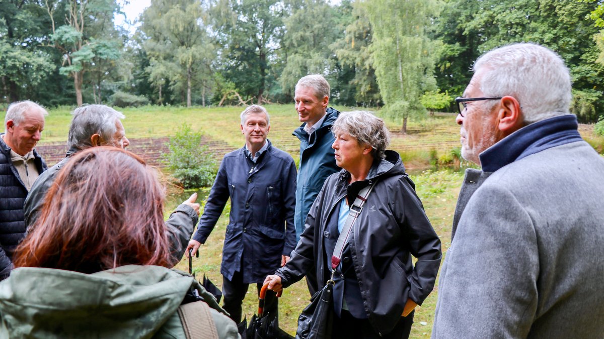 Landtagspräsidentin Hanna Naber steht zwischen mehreren anderen Menschen inmitten grüner Wiesen und Bäume.