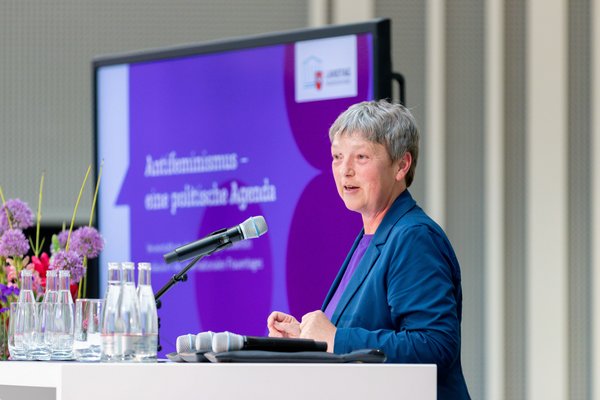 Bild: © Niedersächsischer Landtag Seitliche Ansicht von Landtagspräsidentin Hanna Naber am Mikrofon. Im Hintergrund ist ein Bildschirm mit dem Titel der Veranstaltung zu sehen.