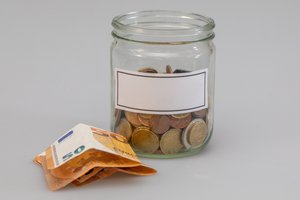 Münzen im Glas und danebenliegende Geldscheine