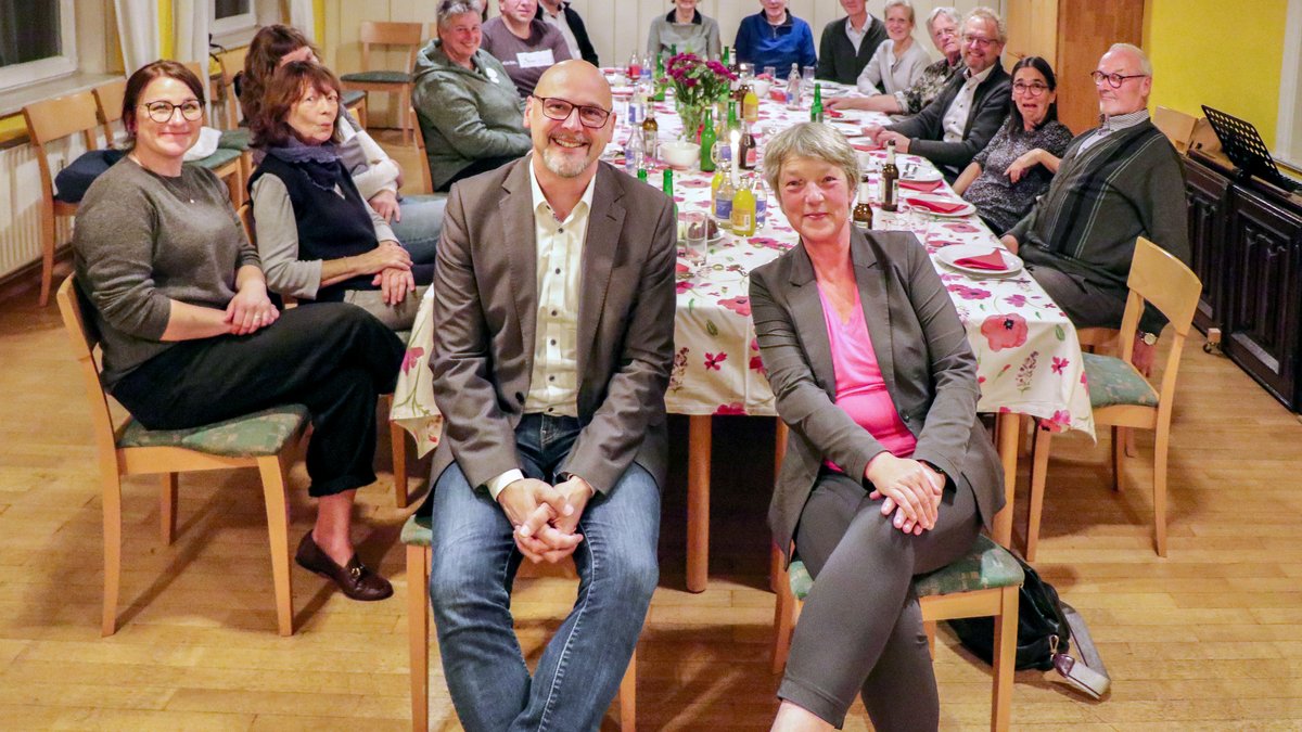 Landtagspräsidentin Hanna Naber und der Wahlkreisabgeordnete Alexander Saade sitzen nebeneinander, hinter ihnen ist eine lange, bunt gedeckte Tafel mit vielen Menschen des Bündnisses zu sehen. Alle lächeln in die Kamera.