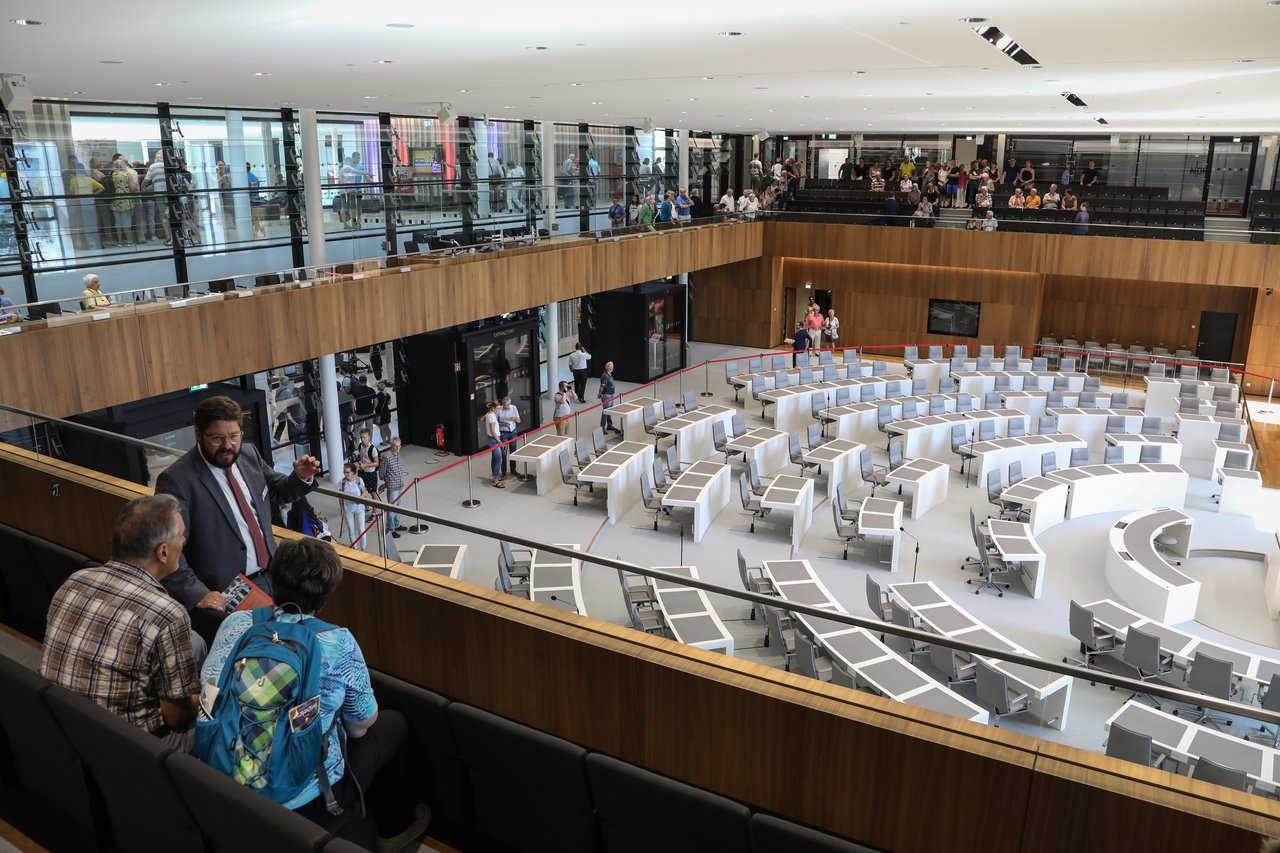 Besucherinnen und Besucher erhalten auf der Besuchertribüne von einem Landtagsmitarbeiter Informationen über das Parlament.