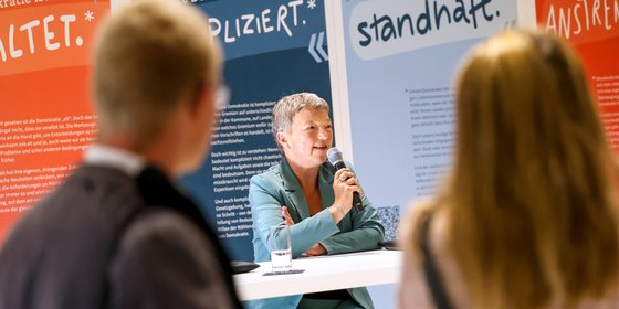 Landtagspräsidentin Hanna Naber vor bunten Aufstellern, im Gespräch mit dem Publikum.