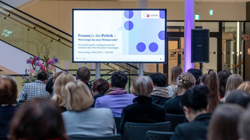 Blick aus dem Publikum auf einen Bildschirm mit dem Titel der Veranstaltung: Frauen(in der)Politik - Was bringt die neue Wahlperiode?