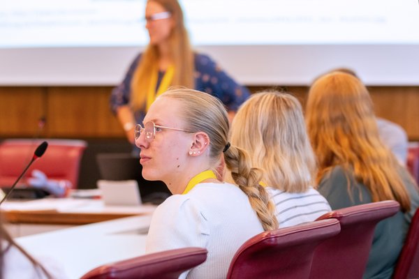 Klick auf das Bild öffnet eine vergrößerte Ansicht in einem Overlay. Zum Schließen des Overlays die ESC-Taste drücken. Drei Jugendlichen an einem Tisch während eines Workshops, im Hintergrund die Workshopleiterin.'}