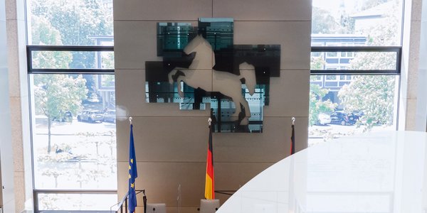 Bild: © Niedersächsischer Landtag; Foto: Stefan Behrens Plenarsaal, darüber das Logo des Niedersächsischen Landtages in abgewandelter Form: Eine 75 ersetzt das Wappen.