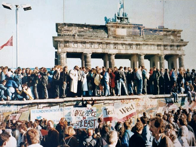Menschenmengen auf der Berliner Mauer Ende 1989 nach dem historischen Mauerfall. Im Hintergrund das Brandenburger Tor, Symbol der Wiedervereinigung Deutschlands.