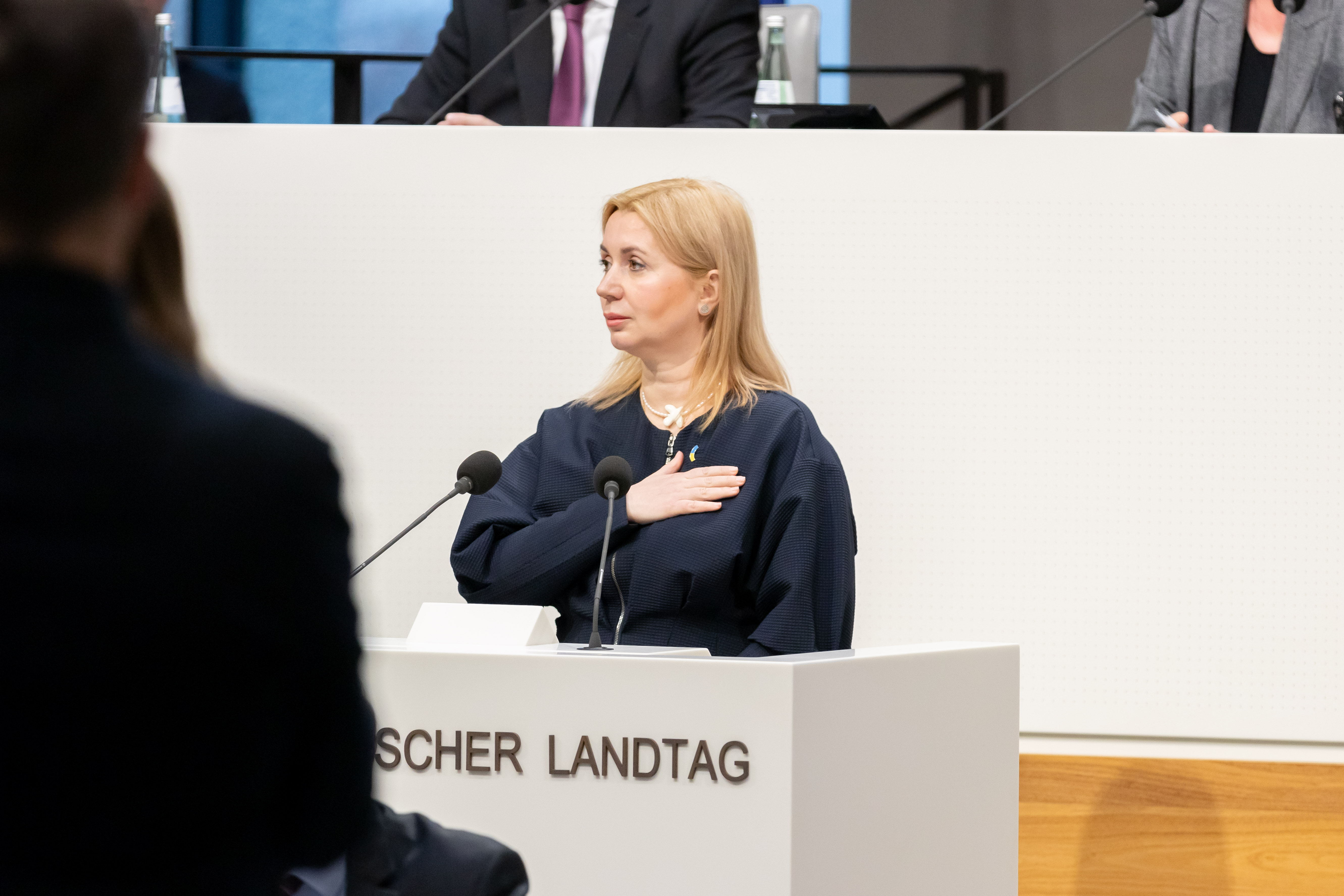 Generalkonsulin Iryna Tybinka steht mit aufs Herz gelegter Hand am Rednerpult des Plenarsaals